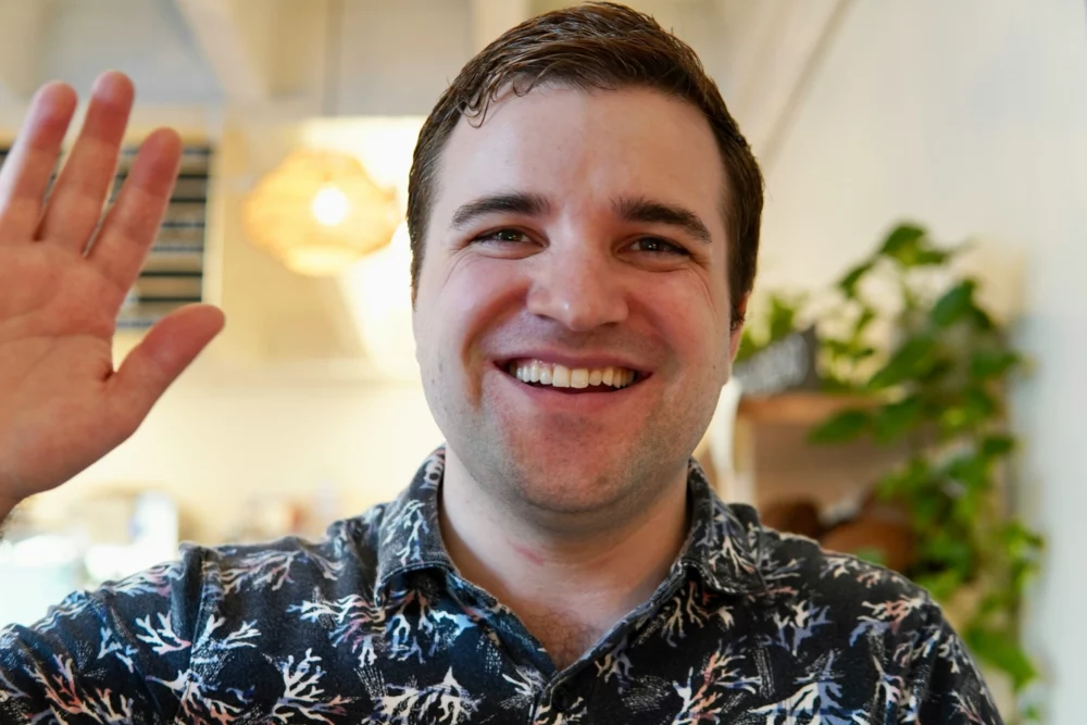 Homme souriant levant la main dans un geste de salutation